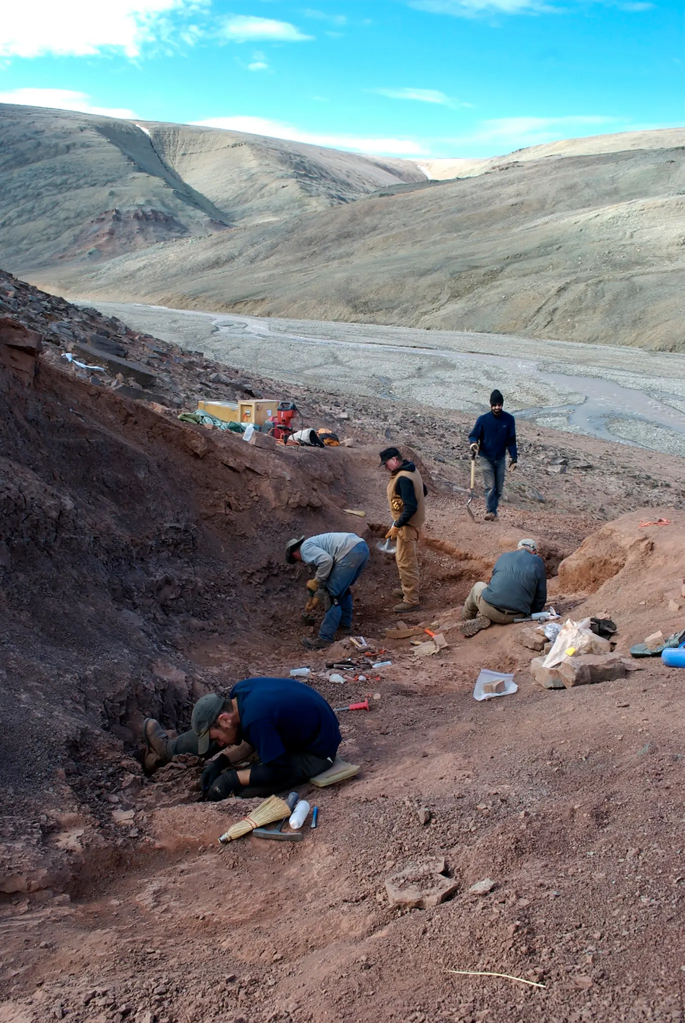 Photo of scientists digging in the dirt on a hillside, looking for fossils