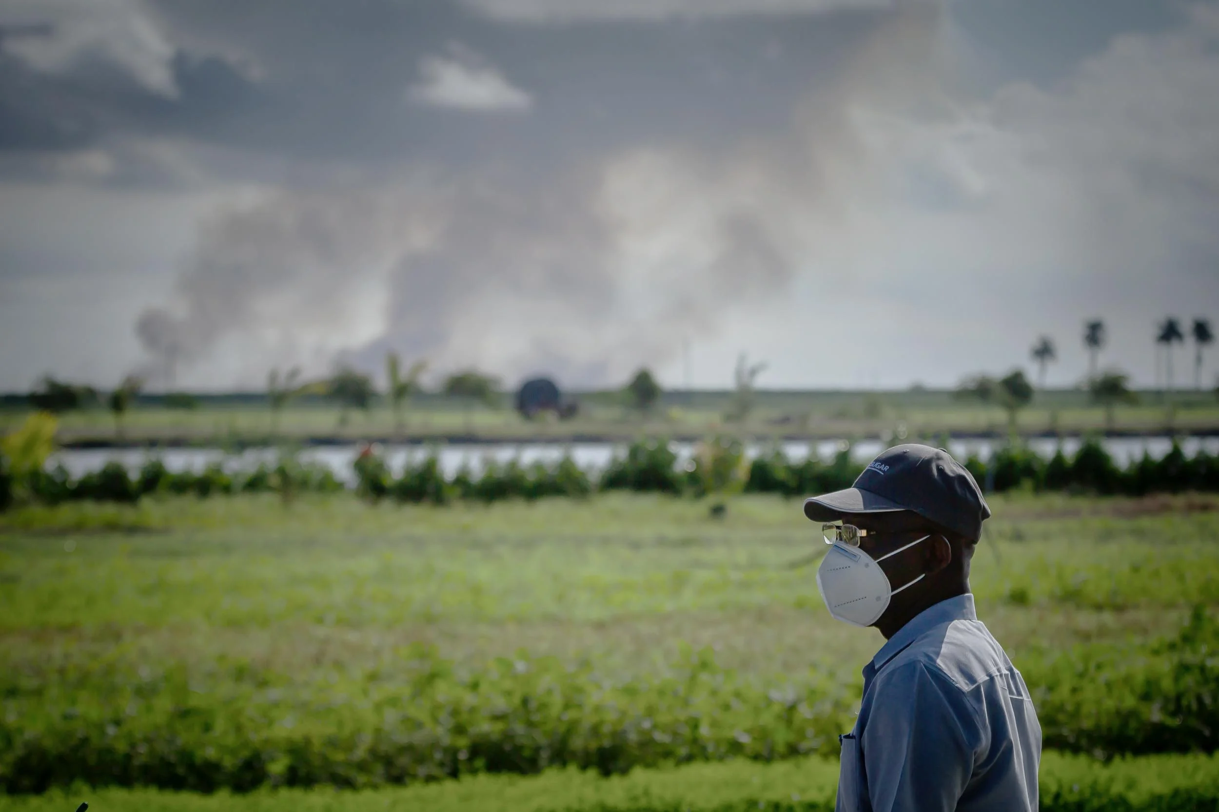 South Bay Mayor Joe Kyles stands in front of sugar cane fields, with smoke visible in the distance.