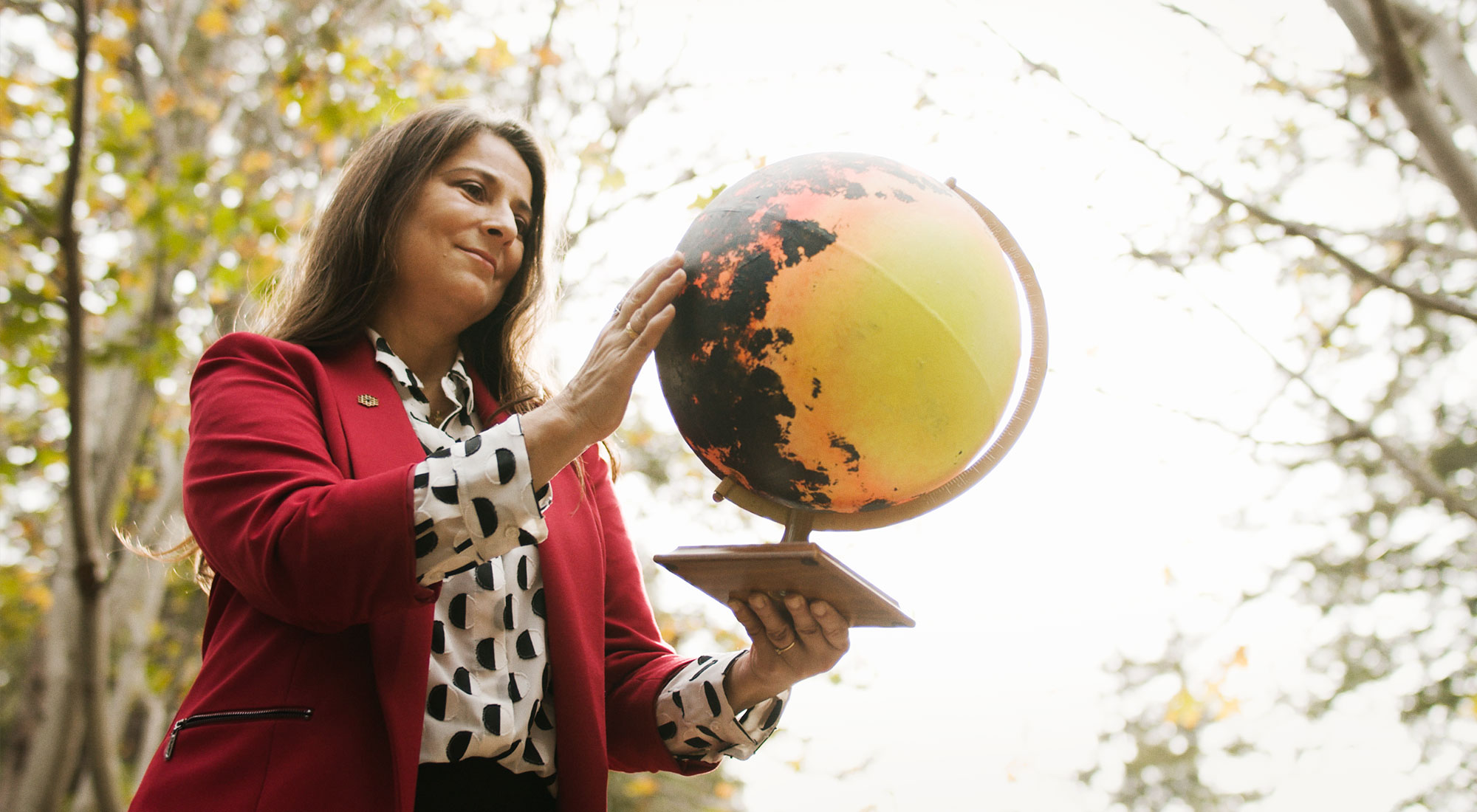 The photo shows Natalie Batalha standing among trees, holding a yellow globe.