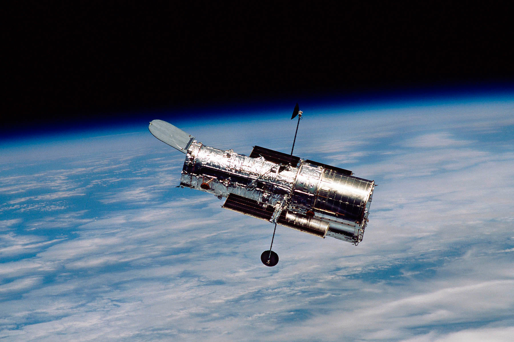 The Hubble Space Telescope flying in low-Earth orbit, with the blue planet visible beneath it.